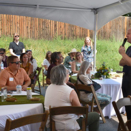 A crowd of people under a tent listen to Colorado Governer Jared Polis speak