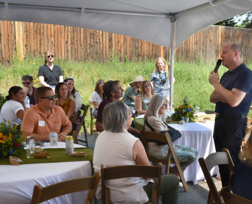 A crowd of people under a tent listen to Colorado Governer Jared Polis speak